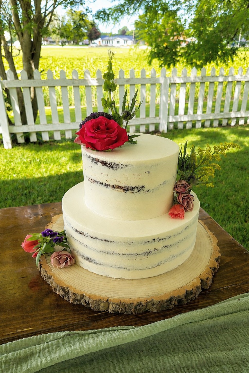 White tiered wedding cake decorated with flowers outdoors